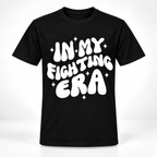 A black short-sleeve crewneck t-shirt with a bold white graphic text reading 'IN MY FIGHTING ERA' surrounded by small white star sparkles, displayed on a clean white background.