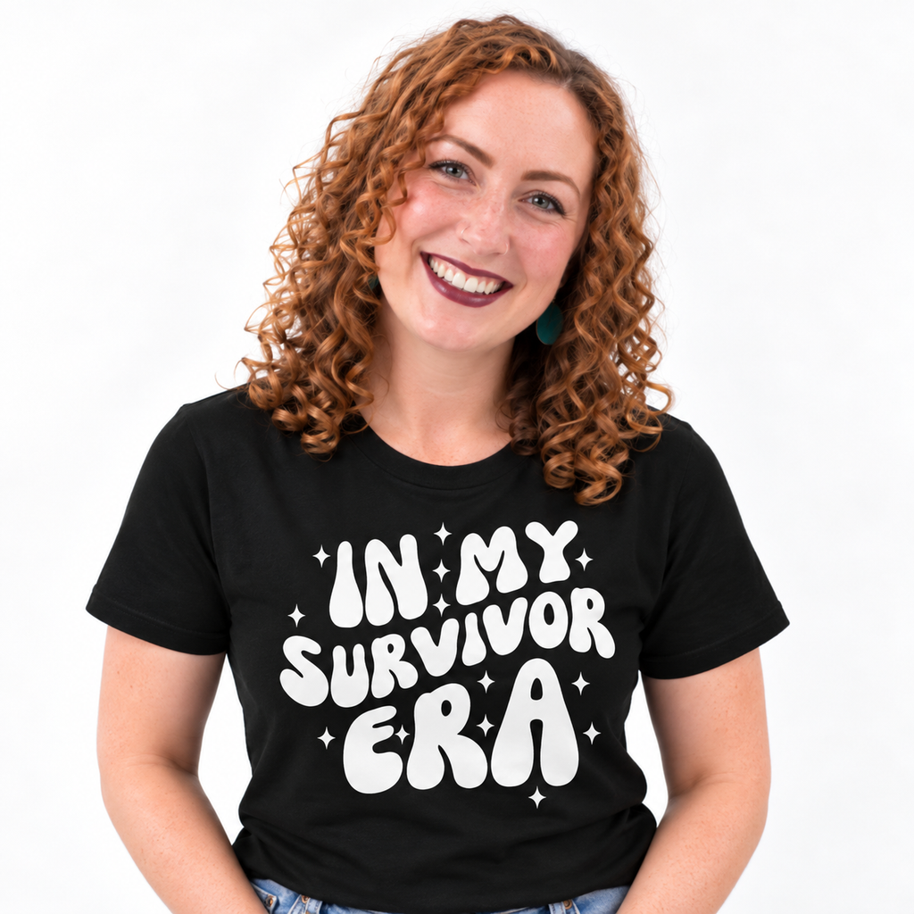 A smiling woman with curly red hair wearing a black t-shirt with the phrase 'IN MY SURVIVOR ERA' printed in a bold white retro font with small star accents, set against a plain white background.