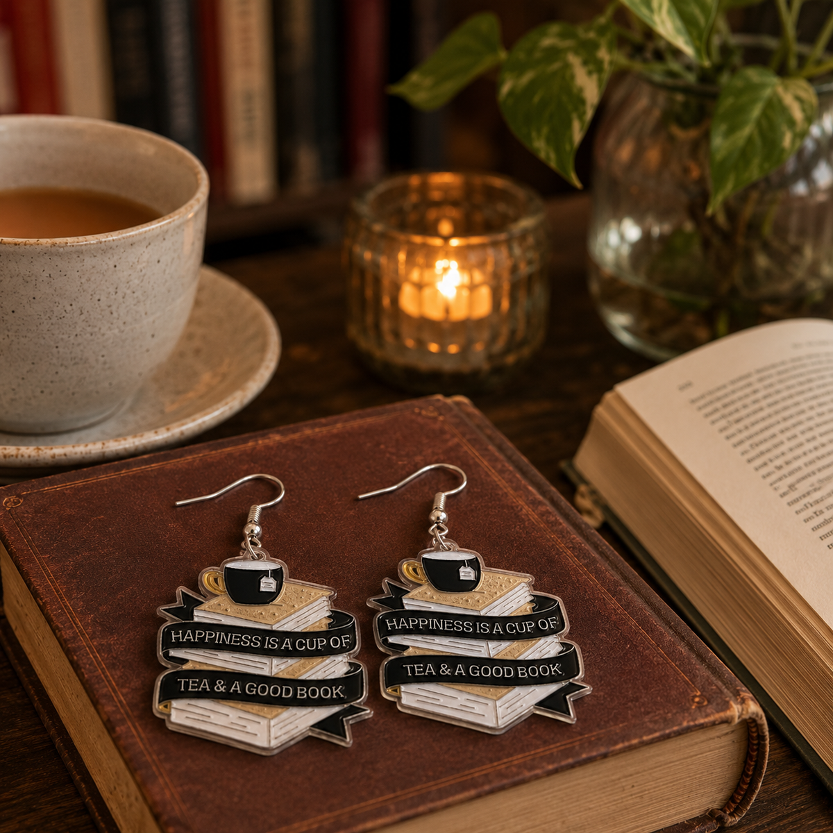 Book Lover Earrings with stacked books, black teacup and Happiness is a cup of tea and a good book quote on a book surrounded by a candle and tea