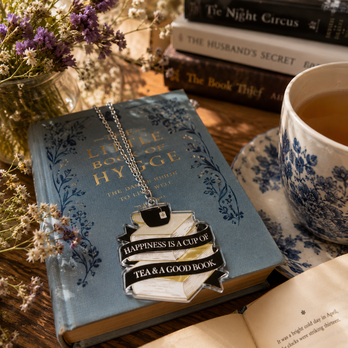 Book Lover Necklace with stacked books, black teacup and Happiness is a cup of tea and a good book pendant over a book surrounded by other books, flowers and tea