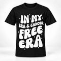 A black short-sleeve crewneck t-shirt with a bold white retro-style graphic reading 'IN MY BRA & CANCER FREE ERA' surrounded by small white star sparkles, shown on a clean white background.
