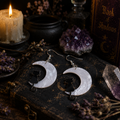 Cat Moon Earrings with black cat silhouettes on pearlescent white crescent moons and silver hooks surrounded by dried flowers, candles and amethyst stones