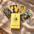 A tarot card deck box labeled 'The Classic Tarot' sits on a beige linen cloth with four illustrated tarot cards fanned behind it.