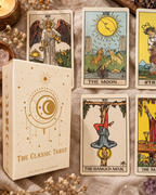 A boxed tarot card deck labeled 'The Classic Tarot' sits beside several illustrated tarot cards on a textured fabric surface, with candles and crystals as styled props.