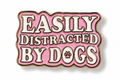 A pink enamel pin with white lettering that reads 'EASILY DISTRACTED BY DOGS' and a small paw print inside the letter O, outlined in gold on a white background.