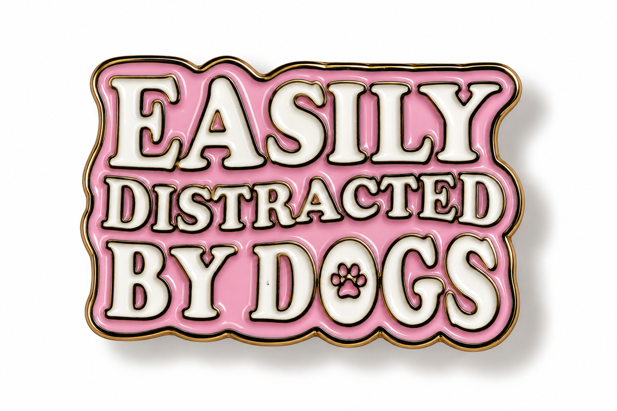 A pink enamel pin with white lettering that reads 'EASILY DISTRACTED BY DOGS' and a small paw print inside the letter O, outlined in gold on a white background.