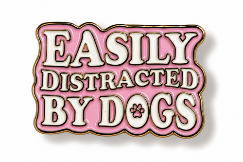 A pink enamel pin with white lettering that reads 'EASILY DISTRACTED BY DOGS' and a small paw print inside the letter O, outlined in gold on a white background.