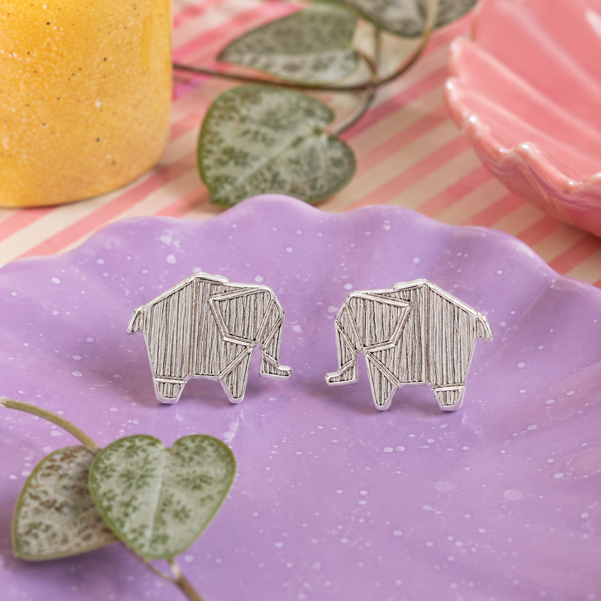 Elephant Stud Earring pair in sterling silver with textured origami-style elephant design on a speckled purple plate with string of hearts plant
