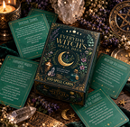 The Everyday Witch's Spell Deck box of 100 spell cards, styled in a mystical flat-lay with surrounding cards, crystals, candles, and brass astrological tools on a dark green fabric background.