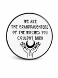 We are the granddaughters of the witches you couldn't burn circle enamel pin. White pin with black writing and border, with a pair of hands and a crescent moon at the bottom