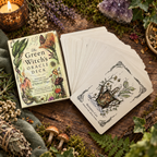 The Green Witch's Oracle Deck box and a fan of cards arranged on a rustic wooden surface with moss, herbs, mushrooms, a candle, and crystals.