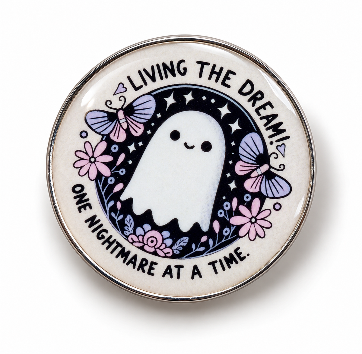 A round enamel pin featuring a cute white cartoon ghost on a dark navy night-sky background, surrounded by pink flowers, purple butterflies, and stars. The text reads 'LIVING THE DREAM! ONE NIGHTMARE AT A TIME.