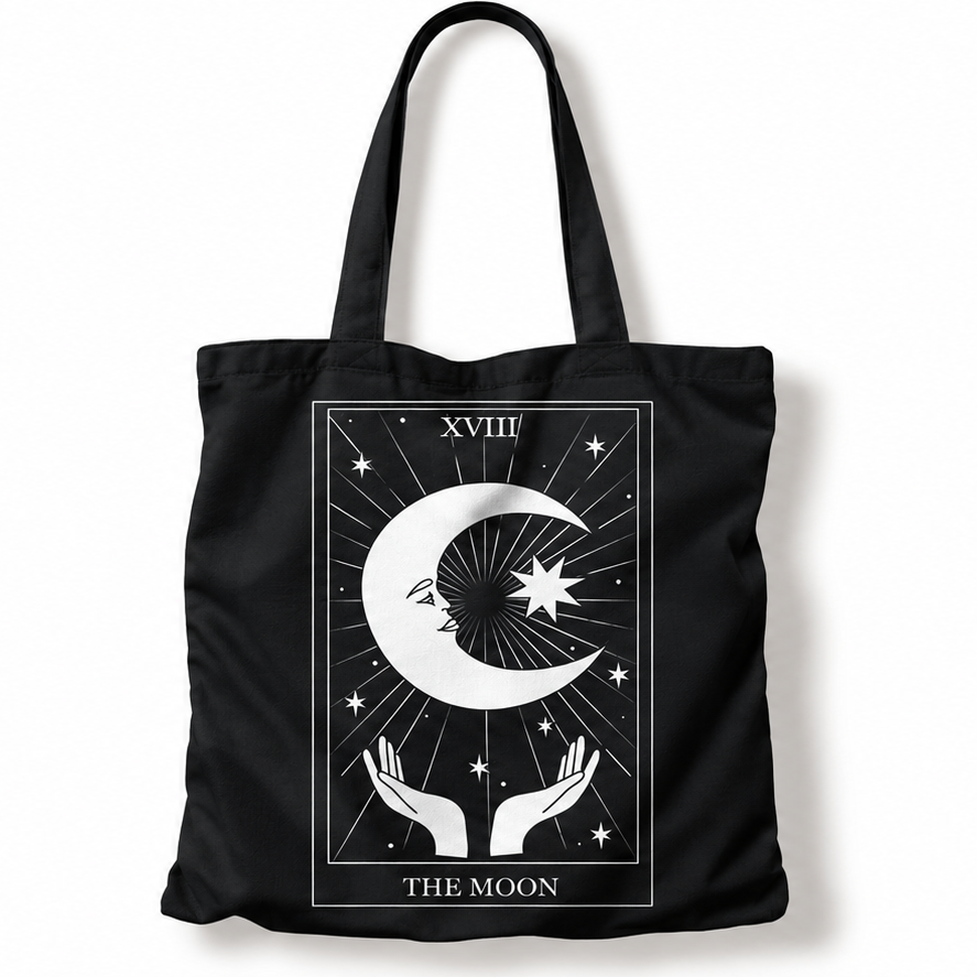 A black canvas tote bag with a white tarot card graphic of 'The Moon' featuring a crescent moon, stars, and hands, shown on a plain white background.