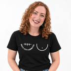 A smiling woman with curly red hair wearing a black short-sleeve t-shirt with a white graphic print that reads 'SHITTY TITTY COMMITTEE' underneath a right mastectomy scar and next to a simplified breast outline. She is photographed against a clean white background.