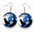 A pair of crescent moon dangle earrings featuring a black cat silhouette set against a blue and yellow swirling night-sky design, with silver fishhook wires above.