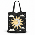 A black canvas tote bag featuring a celestial graphic of a sleeping sun and moon, white clouds, and gold stars on a clean white background.