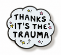 A cloud-shaped enamel pin with a white face, black border, and black text reading 'THANKS IT'S THE TRAUMA' surrounded by small colorful stars on a white background.