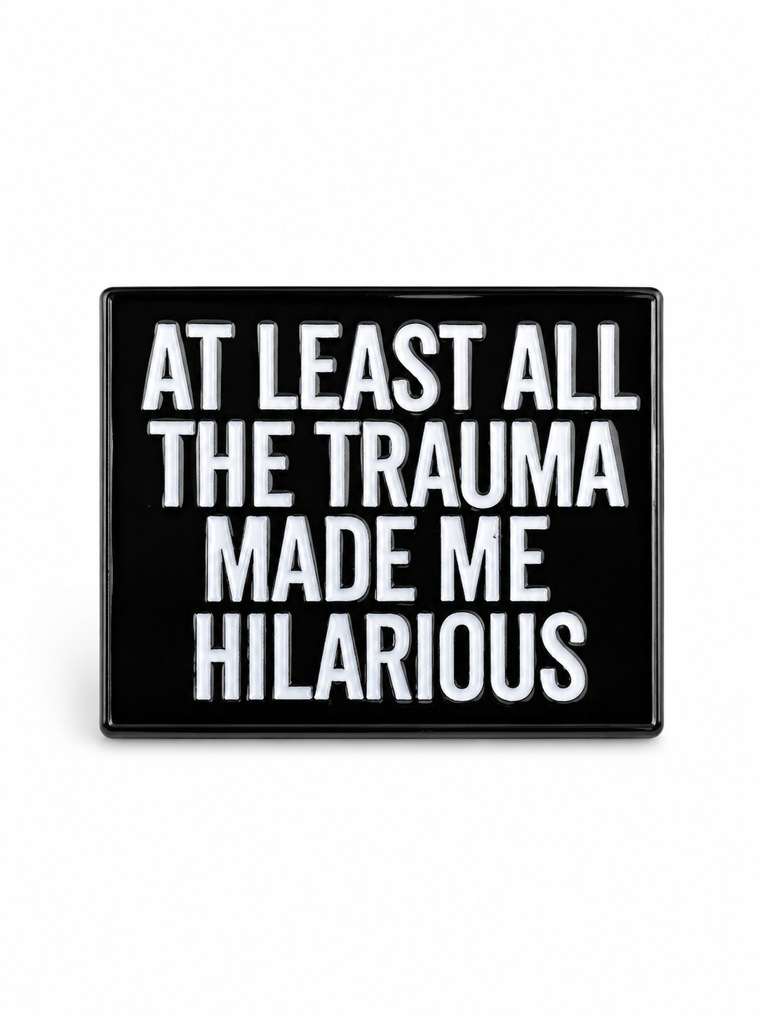 A rectangular black sign or plaque with bold white text reading 'AT LEAST ALL THE TRAUMA MADE ME HILARIOUS' on a plain white background.