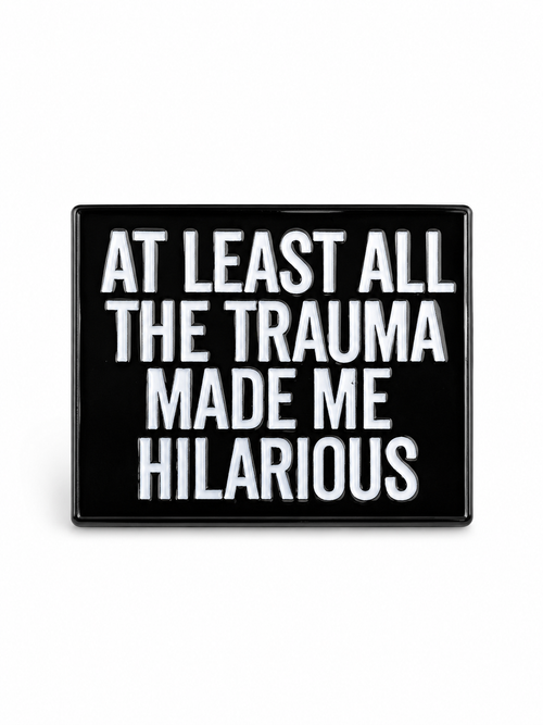 A rectangular black sign or plaque with bold white text reading 'AT LEAST ALL THE TRAUMA MADE ME HILARIOUS' on a plain white background.